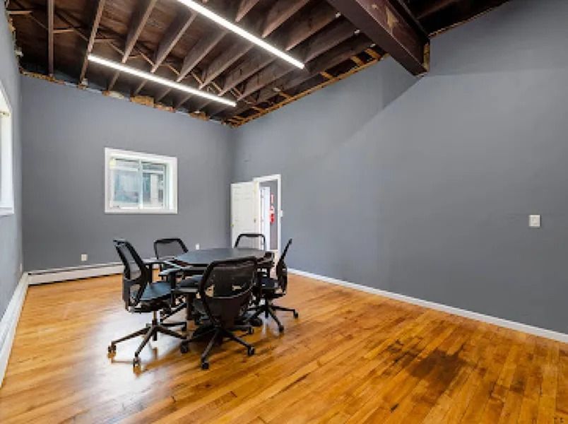 Empty gray room with exposed beams, hardwood floors, and a table with black chairs near a window and door