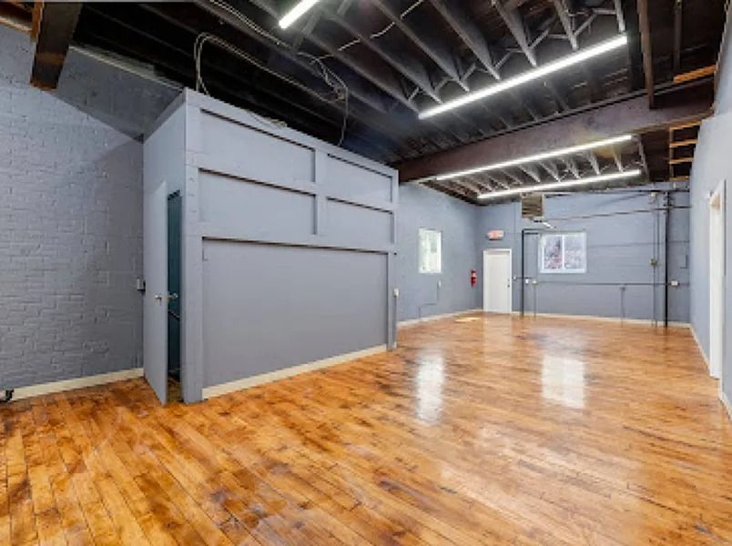 Empty industrial loft with polished wooden floor, gray walls, exposed ceiling beams, and bright overhead lights