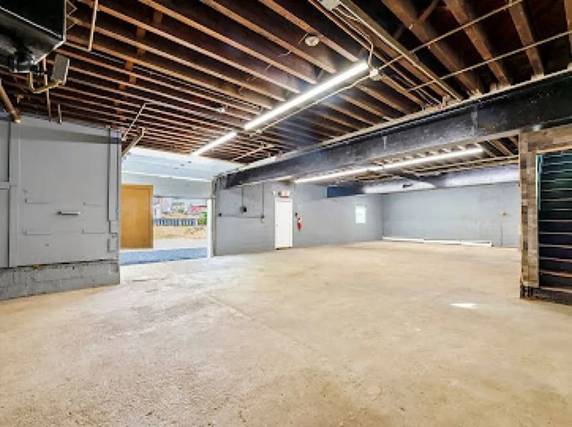 Empty unfinished basement with exposed ceiling beams, concrete floor, and white walls