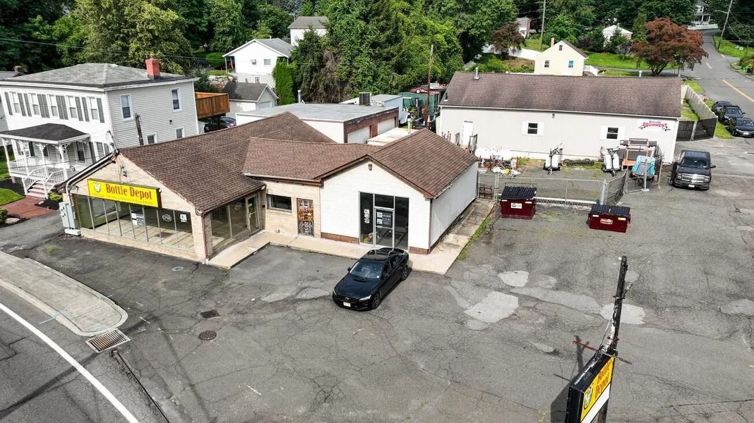 Aerial view of a small commercial building with parked cars and surrounding trees in a neighborhood.