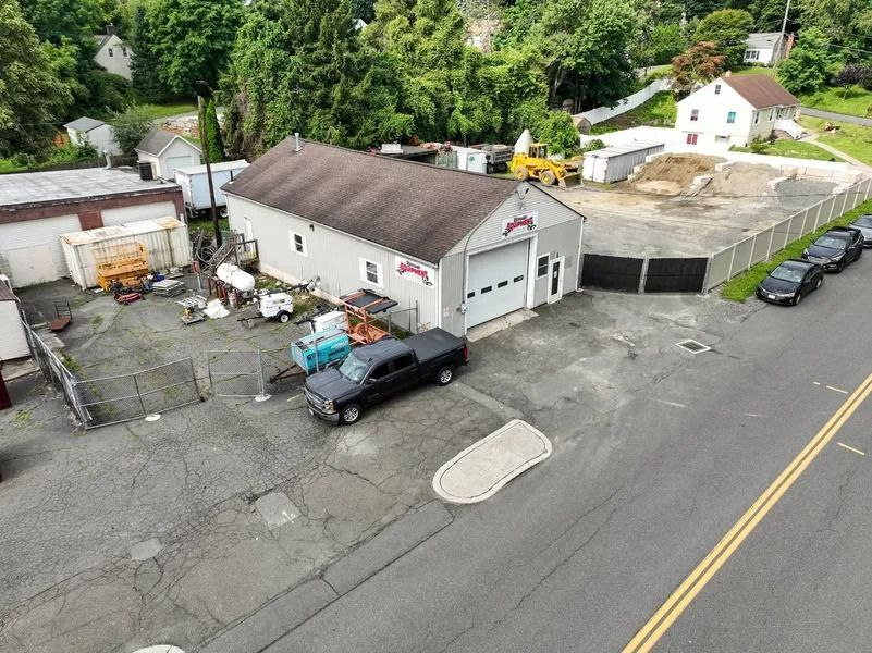 Aerial view of a small industrial lot with parked trucks, a white building, and a road beside it.