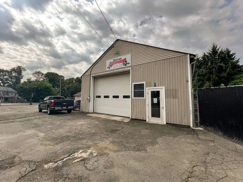 Small tan garage building with a large white overhead door and parked black pickup on a cloudy day.
