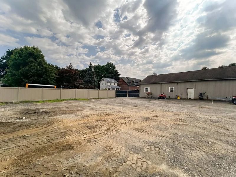 Empty gravel lot beside low white buildings under a cloudy sky