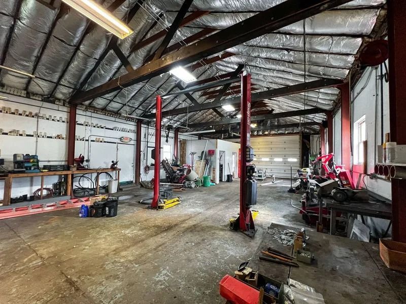 Interior of a cluttered auto repair garage with red lifts, workbenches, tools, and a concrete floor