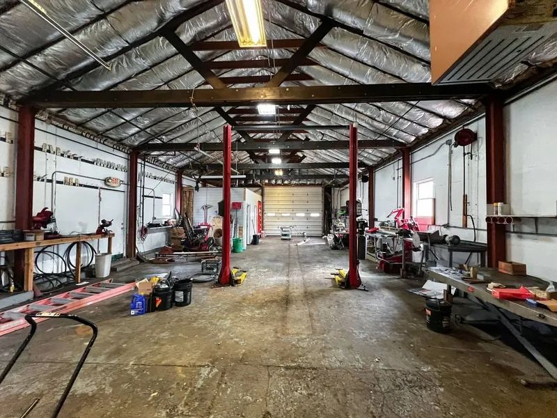 Empty workshop interior with metal beams, tools, and equipment along both sides of a concrete floor