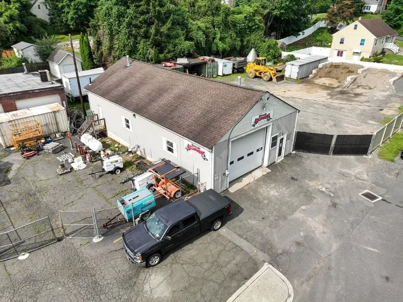 Aerial view of a white industrial garage with parked truck, trailer, and equipment in a yard