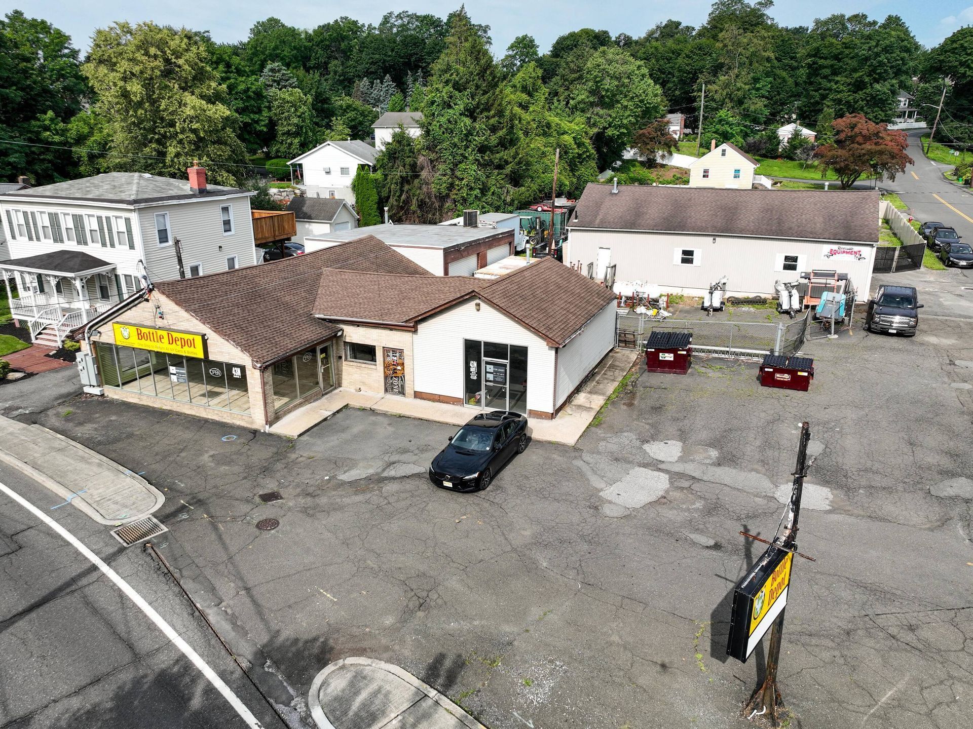 Aerial view of a small roadside building with parked cars and trees behind it.