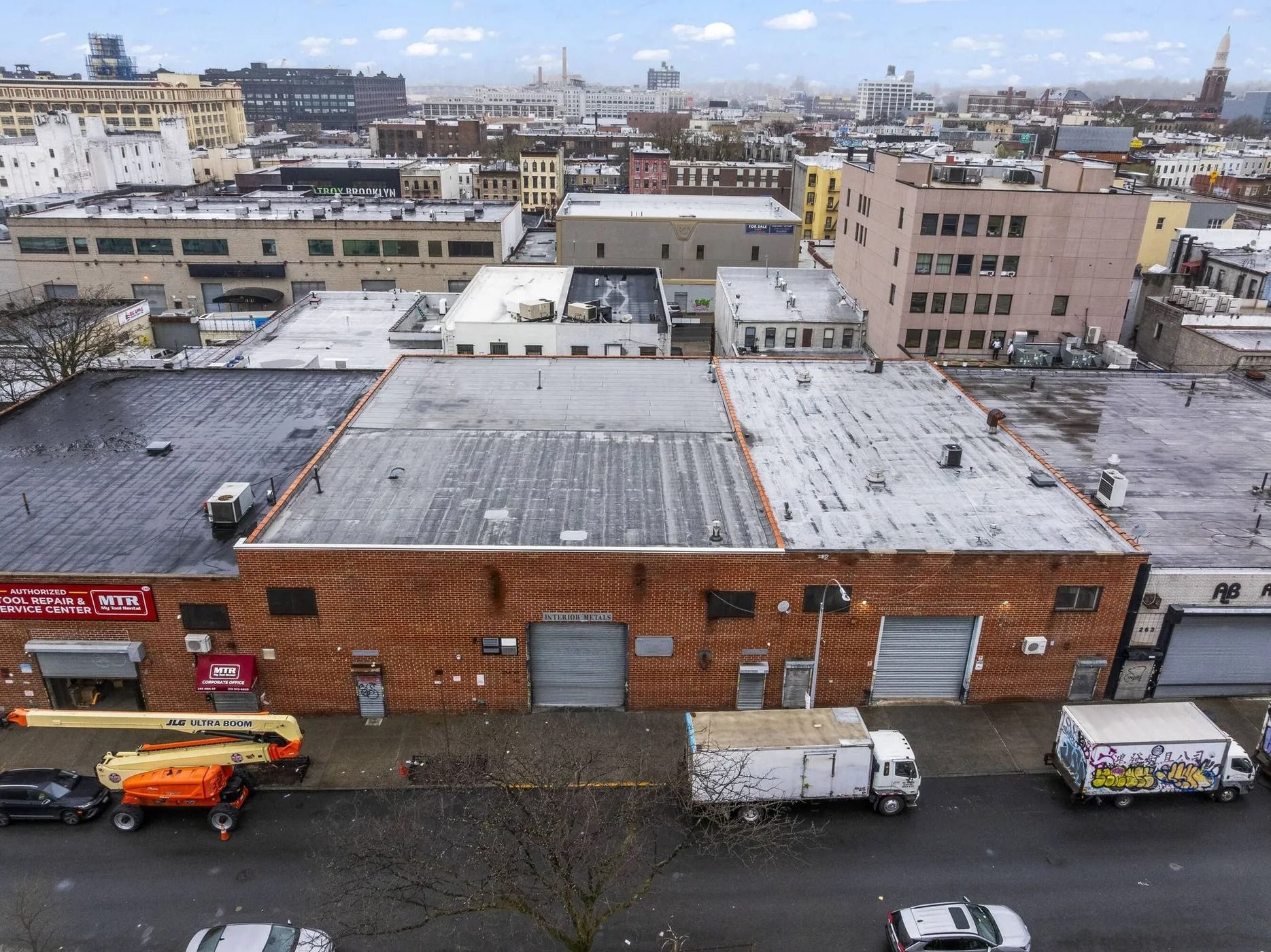 Snow-dusted rooftops and brick warehouses in an industrial cityscape with trucks below.