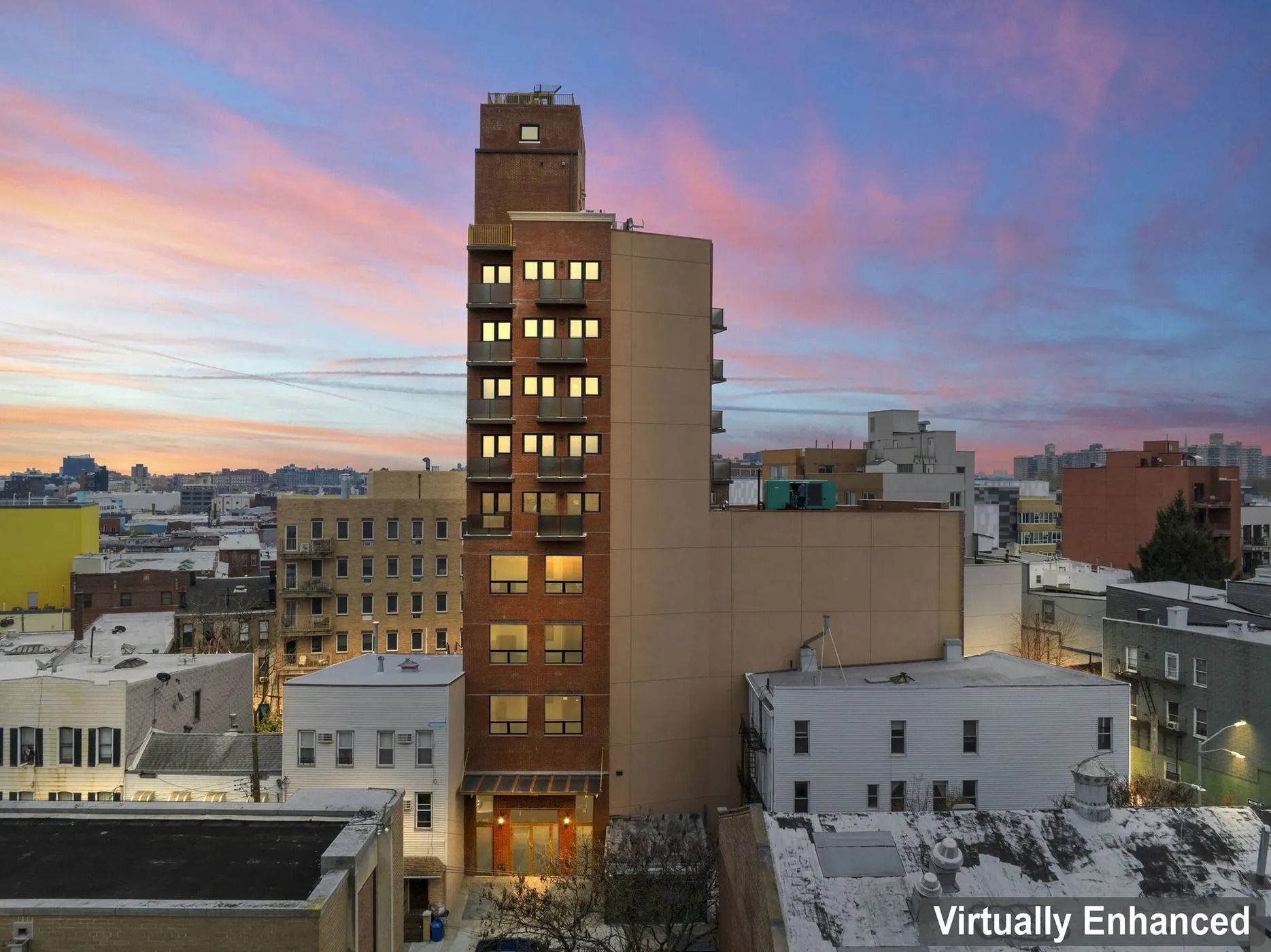 Downtown city skyline at sunset with a tall lit brick tower and pink-blue sky