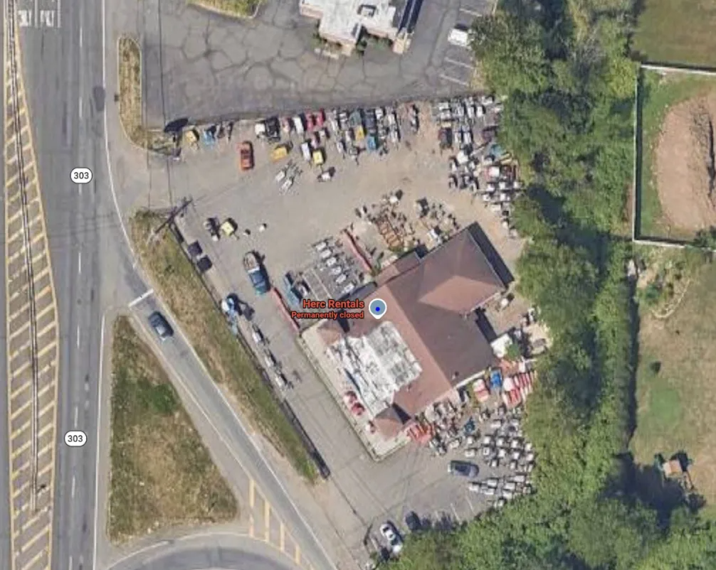 Aerial view of a roadside parking lot beside a building, with many parked cars and surrounding greenery.