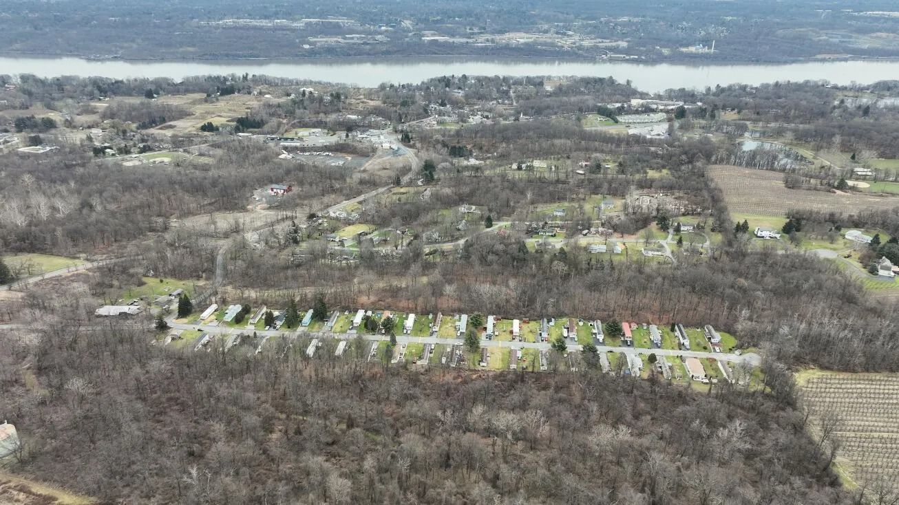 Aerial view of a wooded landscape with a row of houses and water in the distance