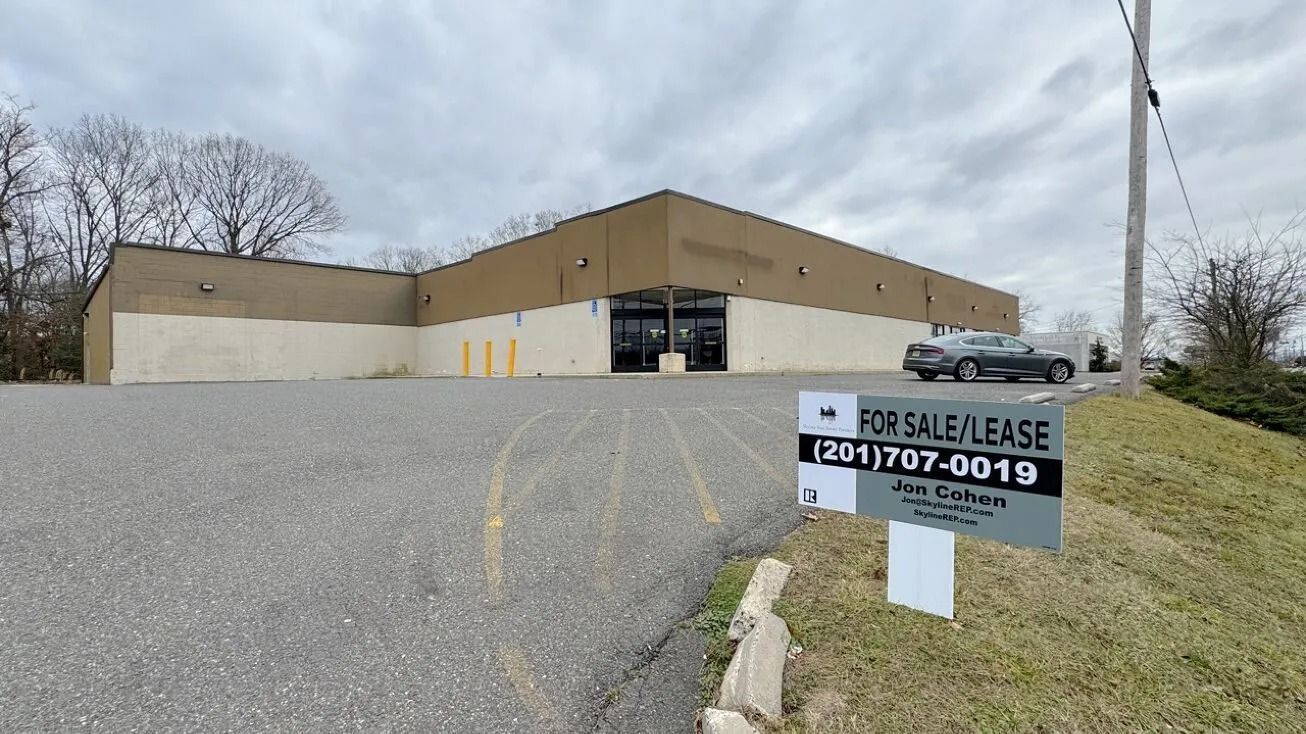 Vacant beige commercial building on a gravel lot with a for-lease sign in front.