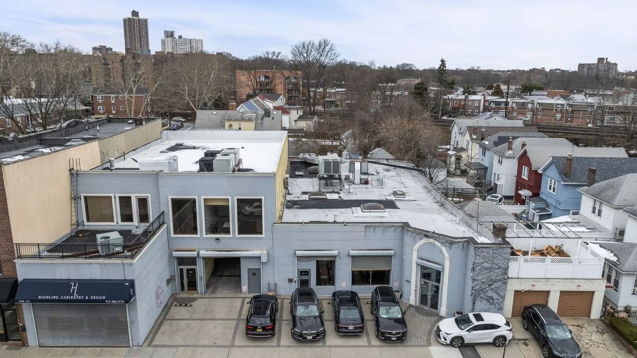 Aerial view of a white building with parked cars and a city neighborhood in the background