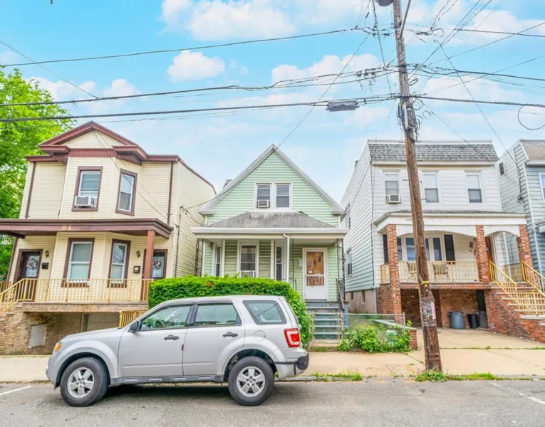 Three small houses on a street with a silver SUV parked in front under utility wires.