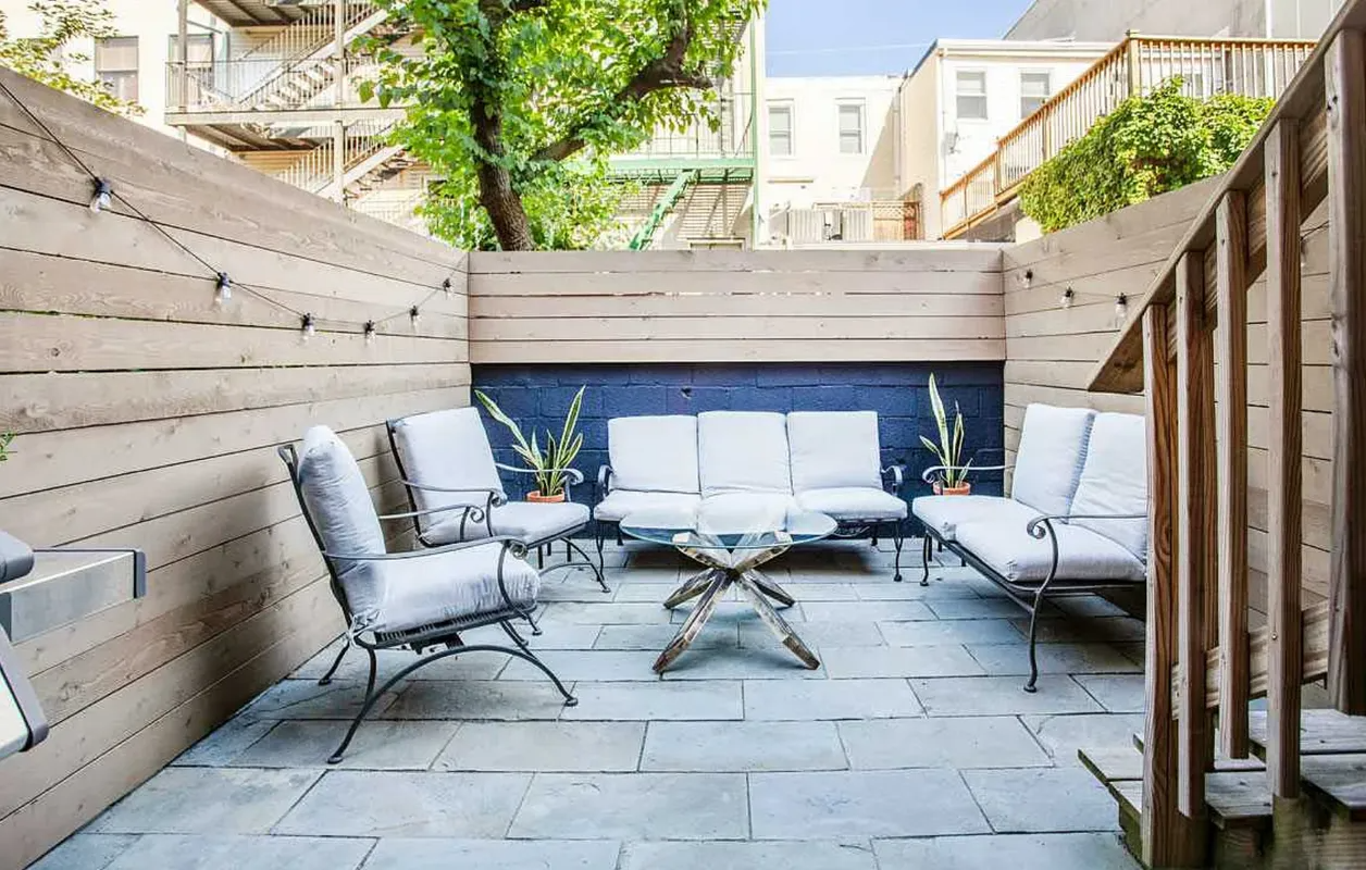 Patio seating area with gray lounge chairs, stone flooring, and wooden privacy walls surrounding a small table