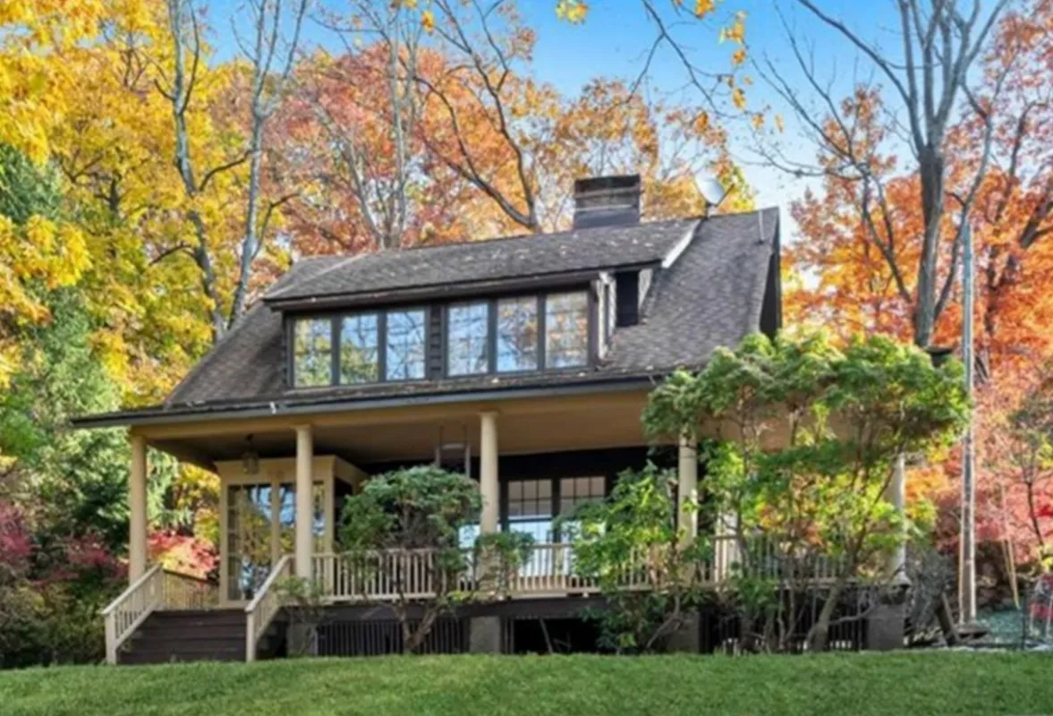 House with wraparound porch amid autumn trees and colorful fall foliage