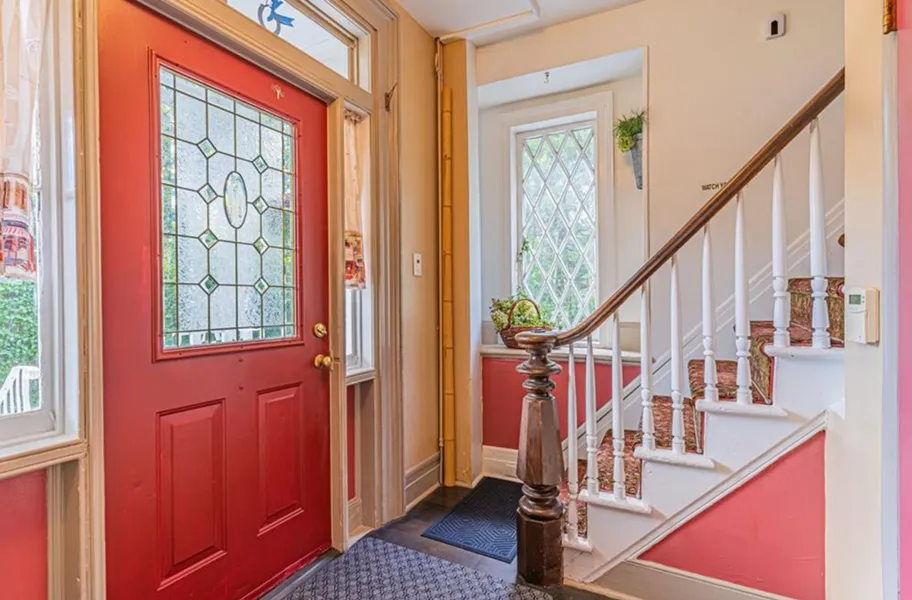 Entryway with a red front door, staircase, and potted plant in a bright hallway