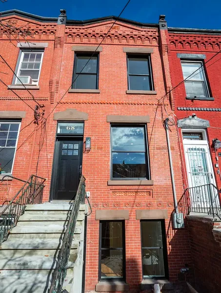 Red brick rowhouses with stoops and black-and-white doors in bright sunlight.