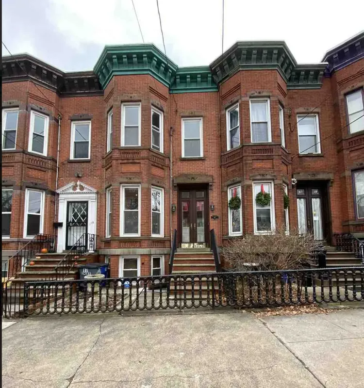 Row of red brick townhouses with white trim and green roof accents behind a metal fence