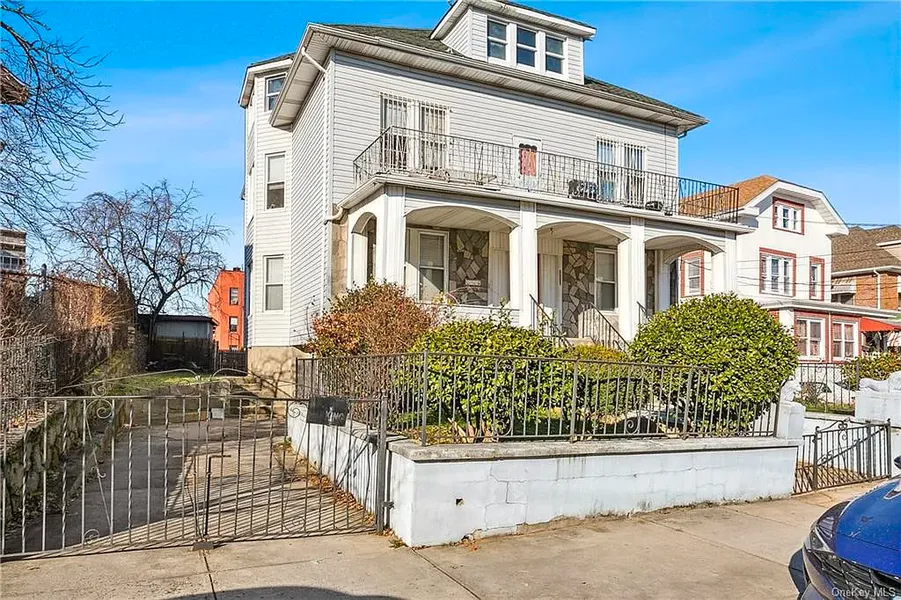 White two-story house with porch, front garden, and gated driveway on a sunny street