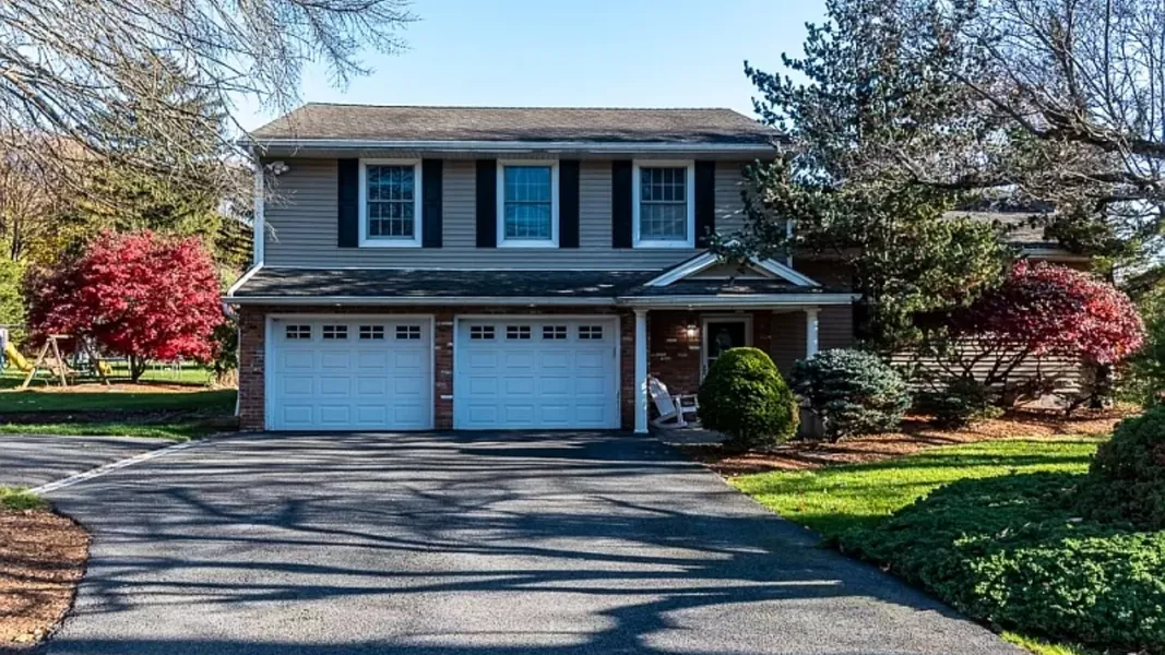Two-story suburban house with a double garage, framed by trees and a driveway in front