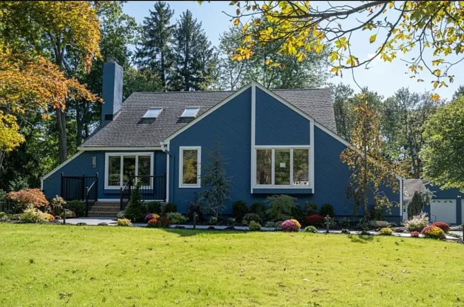 Blue house with white trim in a sunny yard, surrounded by trees and shrubs