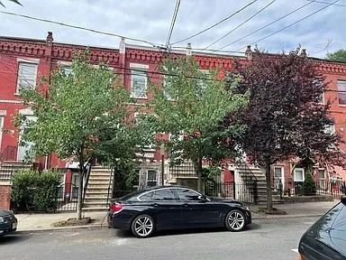 Red brick rowhouses with trees and parked cars along a city street