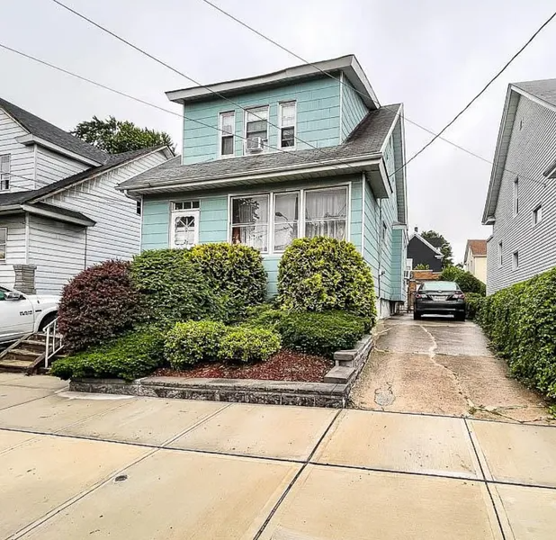 Light blue two-story house with shrubs, driveway, and a parked car in the side driveway