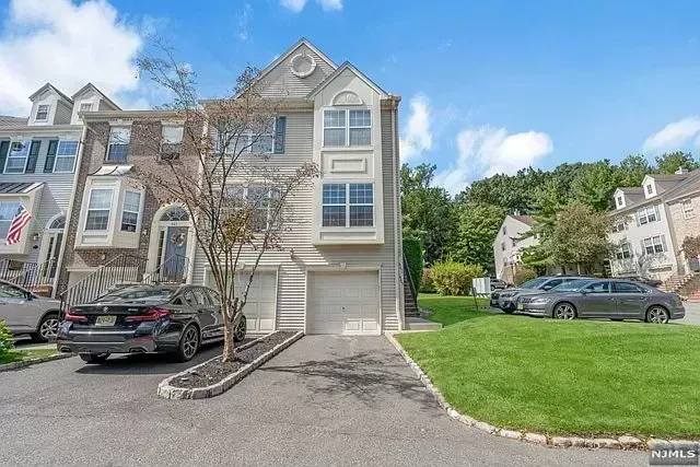Townhouse exterior with garage, parked cars, and green lawn on a sunny day