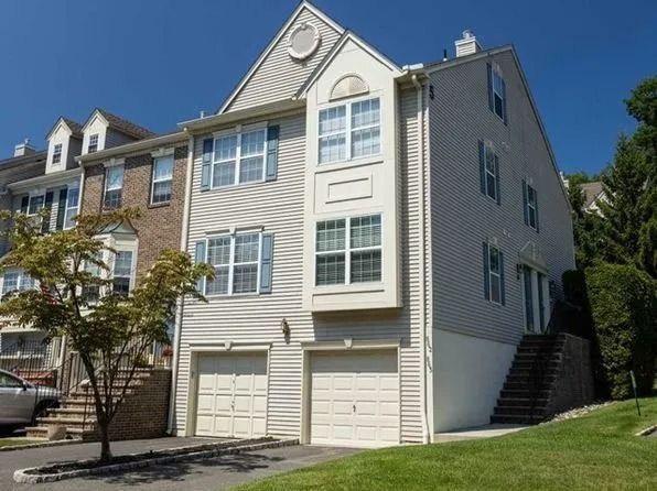 Three-story beige townhouse with white trim, garage, and side stairway under a clear blue sky