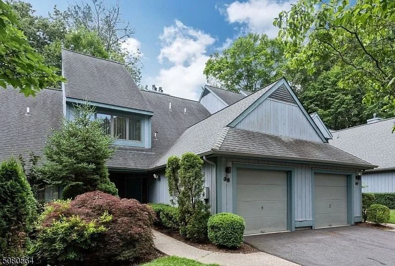 Suburban house with gray roof, garage, and lush green trees and shrubs