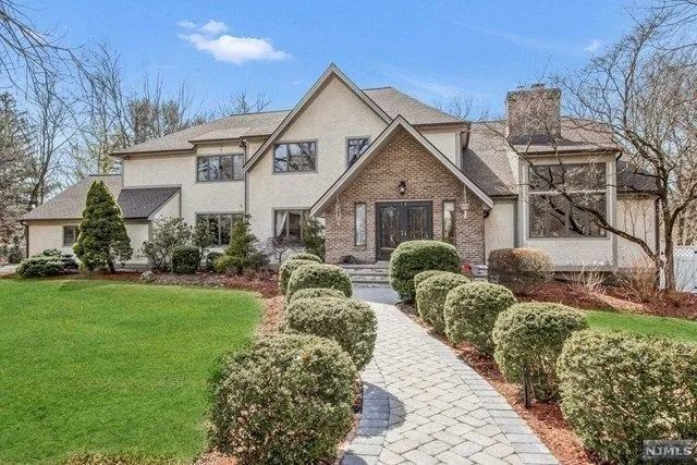 Large beige suburban house with a stone walkway, trimmed shrubs, and a green lawn.