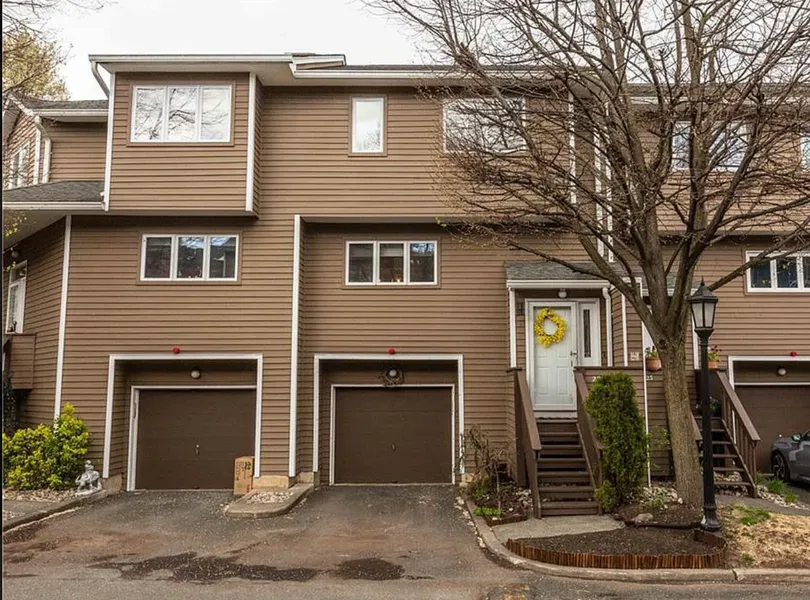 Brown townhouse with two garage doors, front steps, and a leafless tree in front