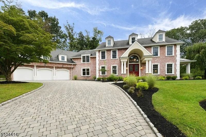 Large brick mansion with a curved driveway, white garage, and manicured lawn under a cloudy sky
