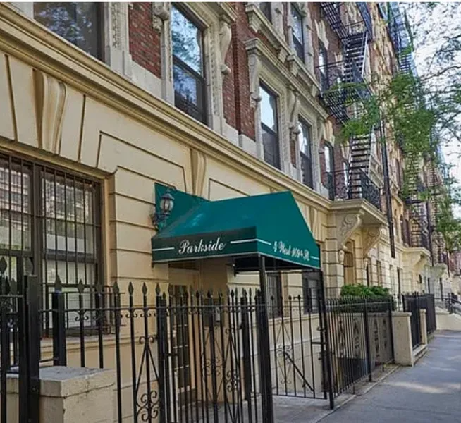 Apartment entrance with green awning along a city sidewalk and iron fence