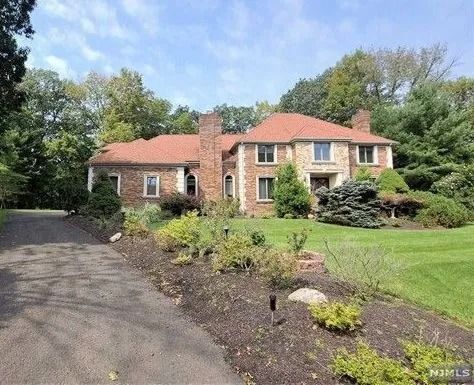 Brick house with red roof, driveway, and landscaped front yard beside trees and lawn