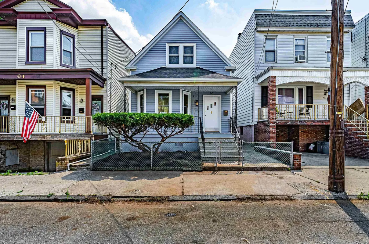 Row of narrow houses with a gray house centered behind a chain-link fence on a city street