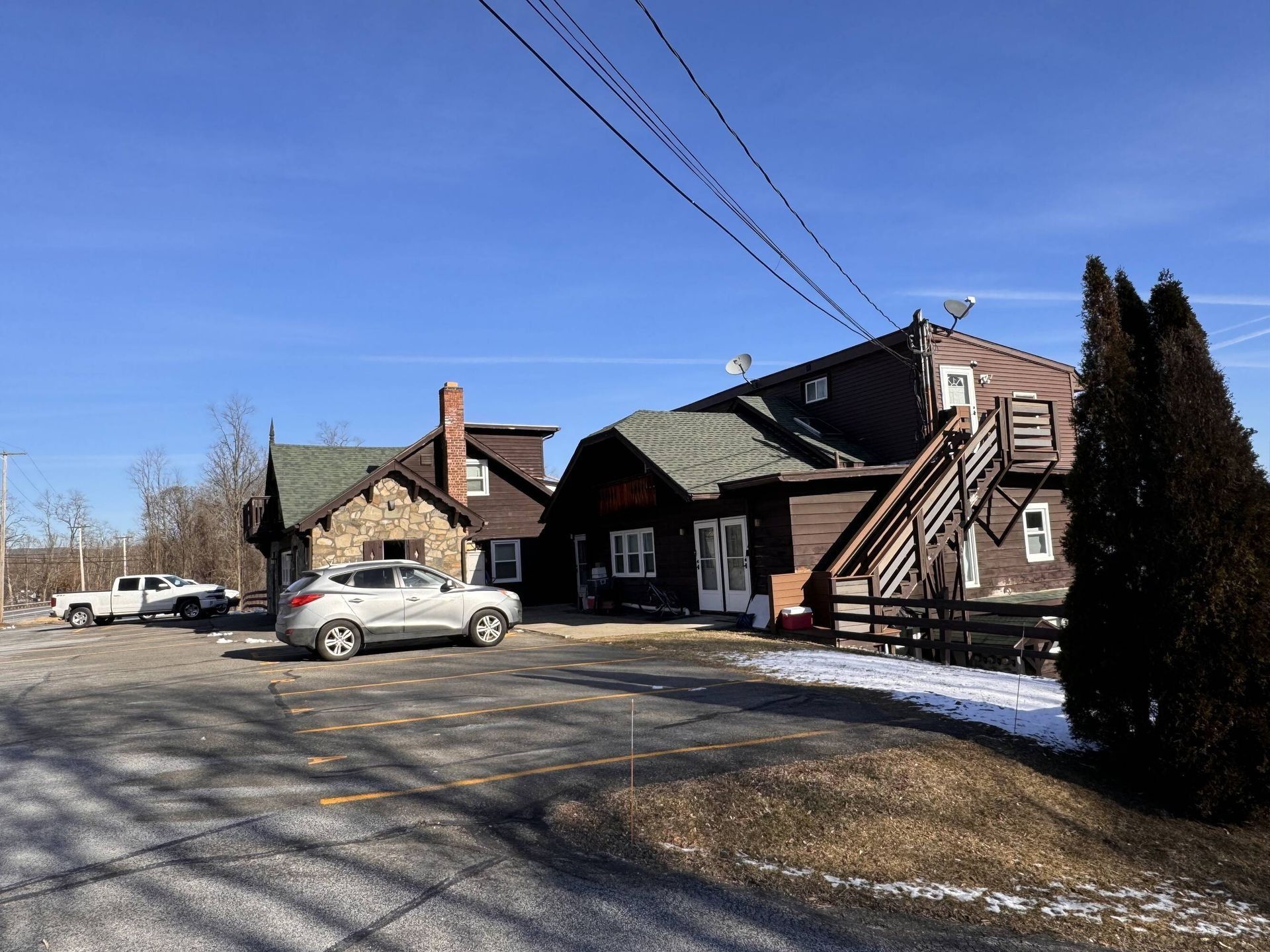 Wooden lodge building with parked cars under a clear blue sky, edged by snow and trees