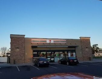 Brick storefront with a striped sign, two parked cars, and a clear blue sky