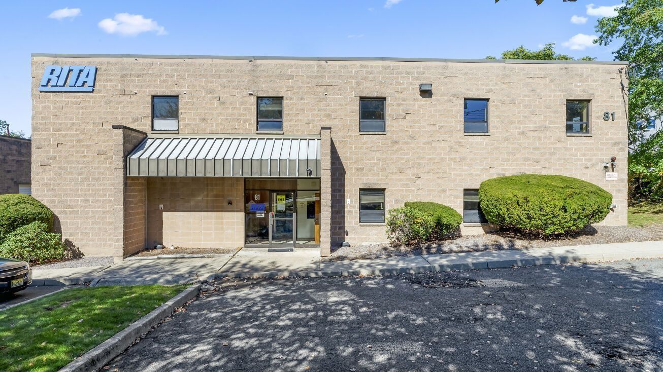 Brick office building with striped awning, glass entrance, and small shrubs in front