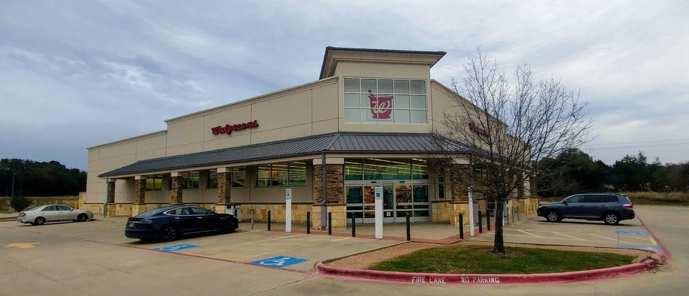 Wide-angle view of a beige retail store with parked cars and a red curb under cloudy skies