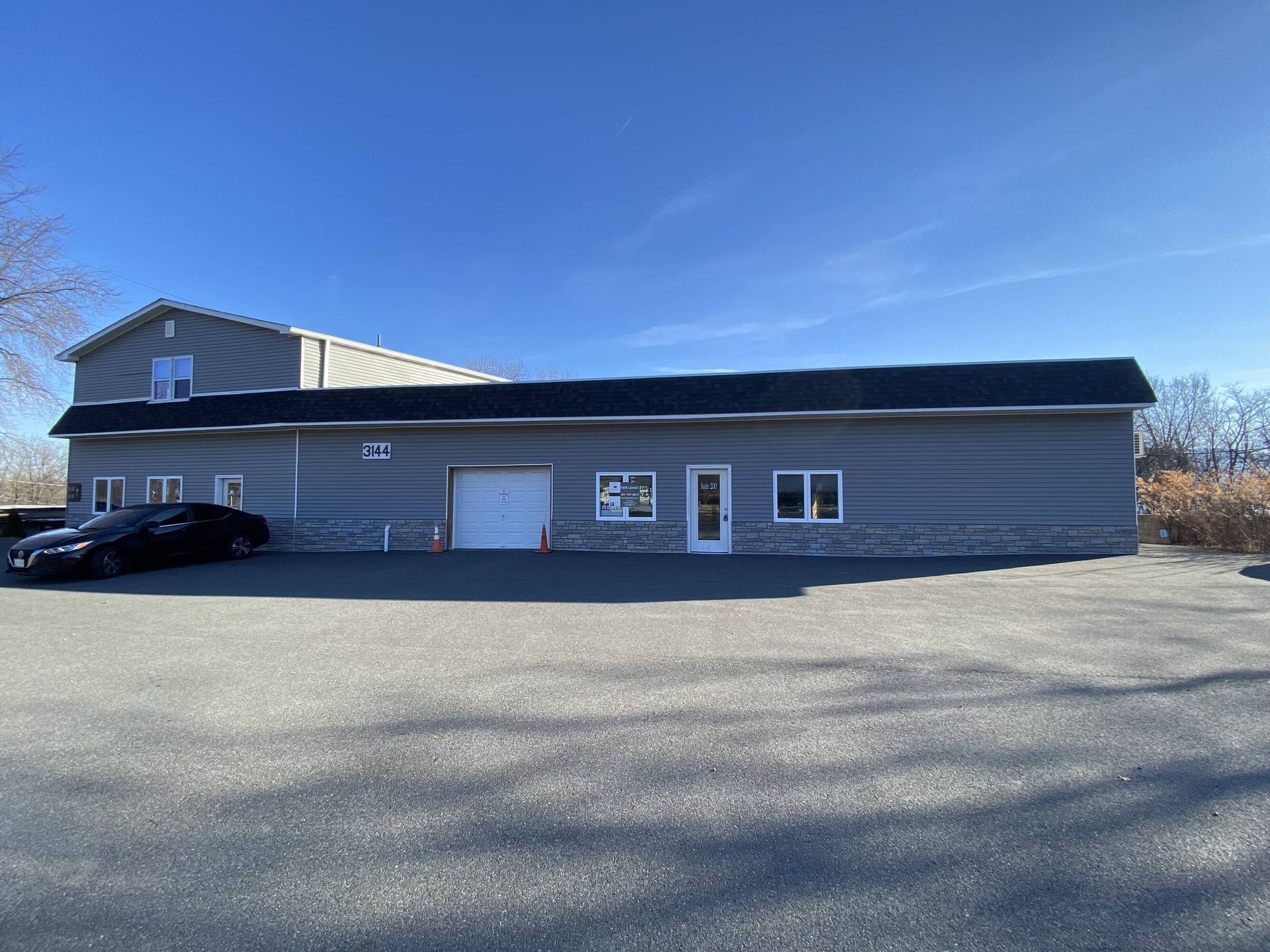 Single-story gray building with a black roof, garage door, and parked car under a clear blue sky.