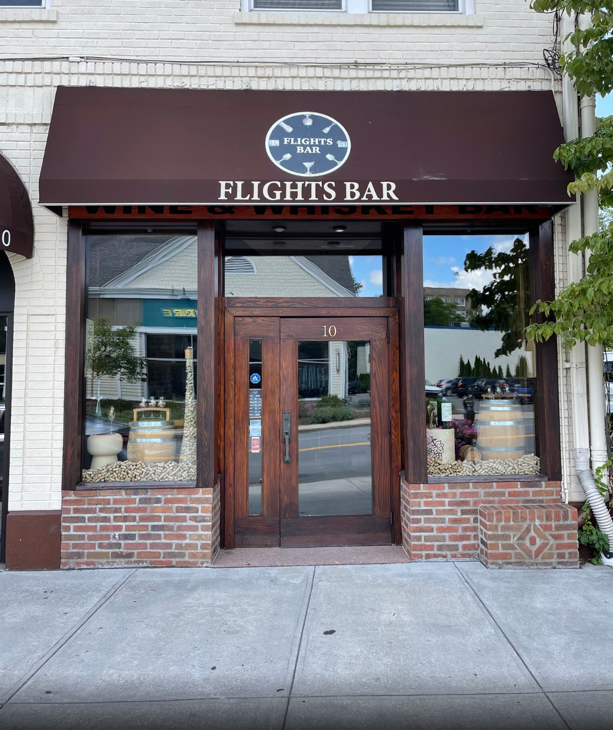 Storefront with a brown awning reading “Flights Bar” and a wooden door on a brick sidewalk.