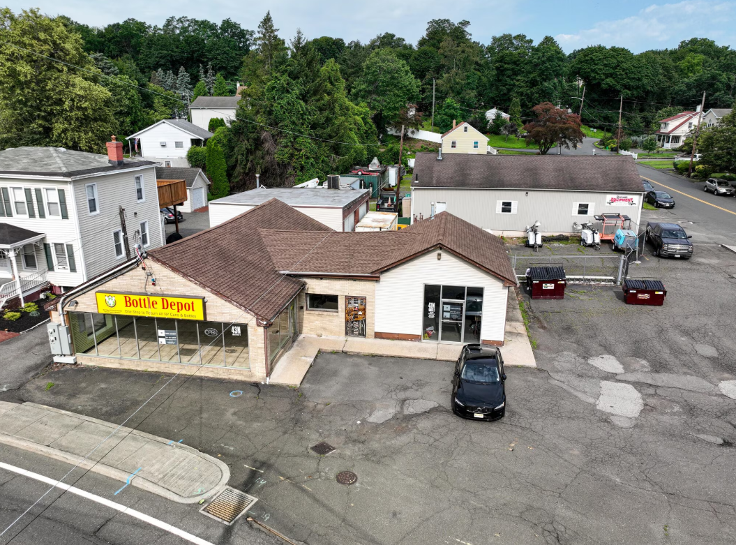 Aerial view of a small commercial building with parked cars and nearby houses in a suburban area.
