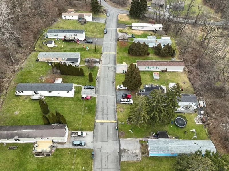 Aerial view of a mobile home park with rows of trailers, driveways, and trees along a central road.
