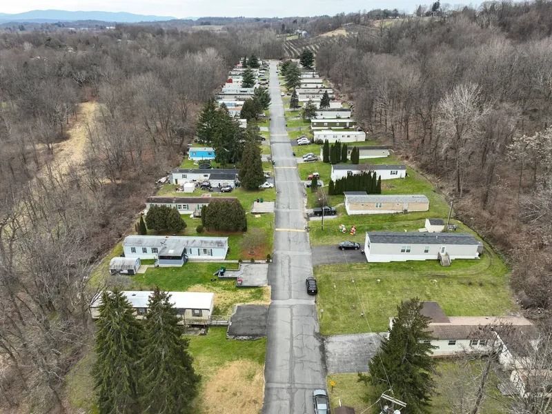 Aerial view of a mobile home park with a straight road, trailers, lawns, and leafless trees.