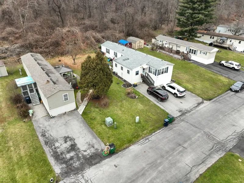 Aerial view of a residential street with mobile homes, parked cars, and a grassy yard.