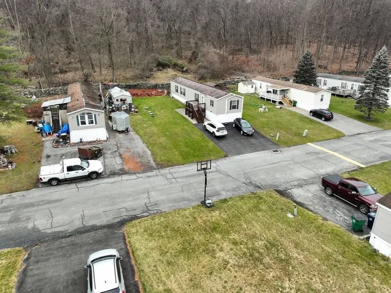 Aerial view of a mobile home park with trailers, parked vehicles, and leafless trees along a road.
