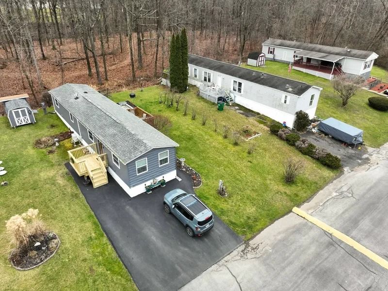 Aerial view of two mobile homes with driveways, parked vehicles, and a wooded yard.