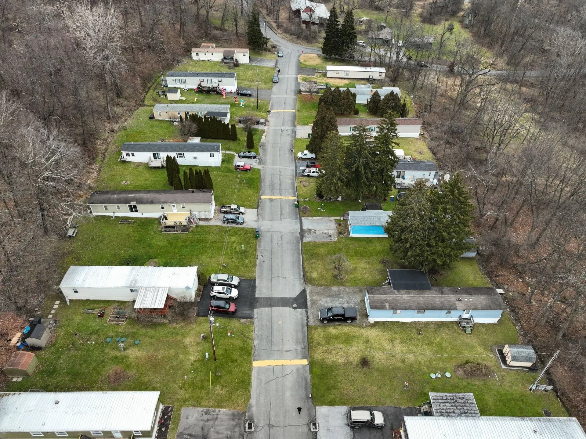 Aerial view of a mobile home park with rows of trailers, a central road, and bare trees.